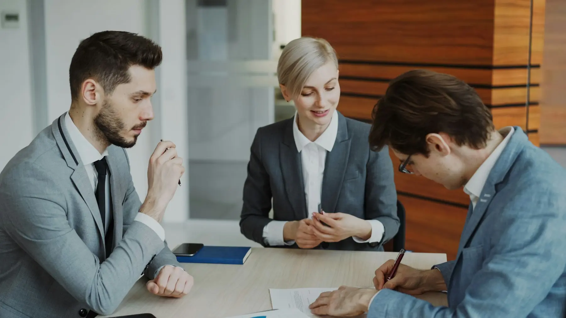 Buyer signing an agreement while two professionals review the documents