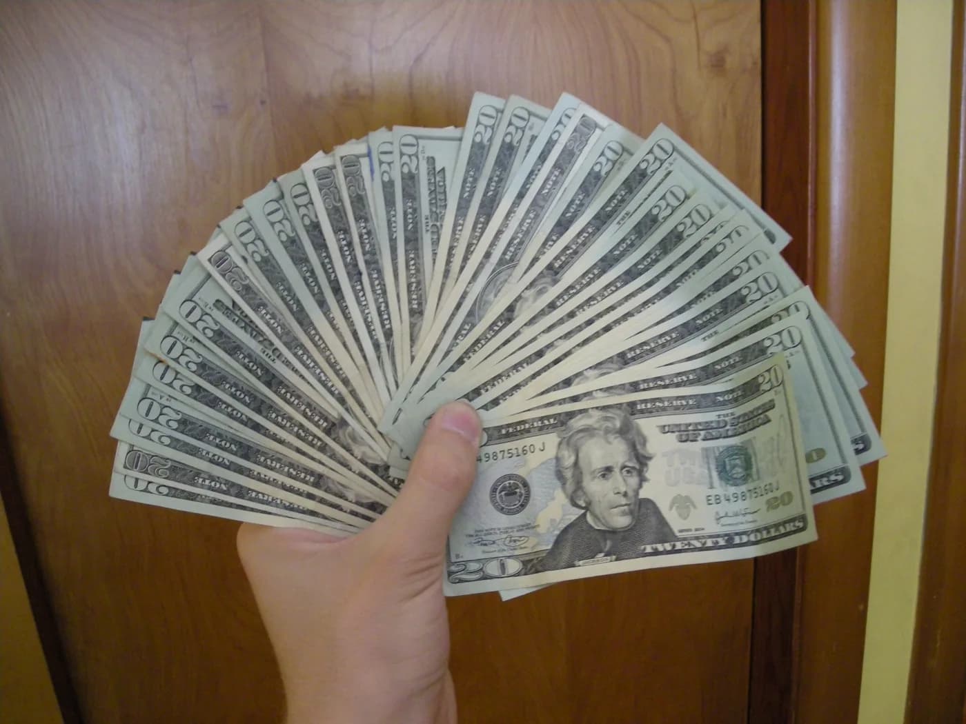 A hand holding a fan of United States twenty-dollar notes